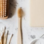 Natural Cleaning Products - Top view composition of wooden cleaning brush and soap and toothbrush and tooth powder and cotton swab placed on marble surface with line chip