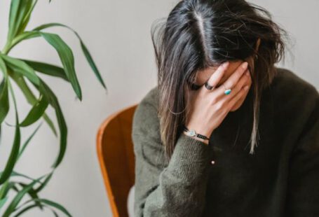 Composting Mistakes - Unrecognizable young upset female millennial with dark hair in stylish sweater covering face with hand while siting on chair at home