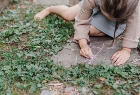 Natural Dyes - High angle of crop unrecognizable barefooted child painting on ground with colorful chalks while playing in green garden