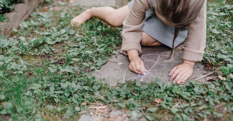 Natural Dyes - High angle of crop unrecognizable barefooted child painting on ground with colorful chalks while playing in green garden